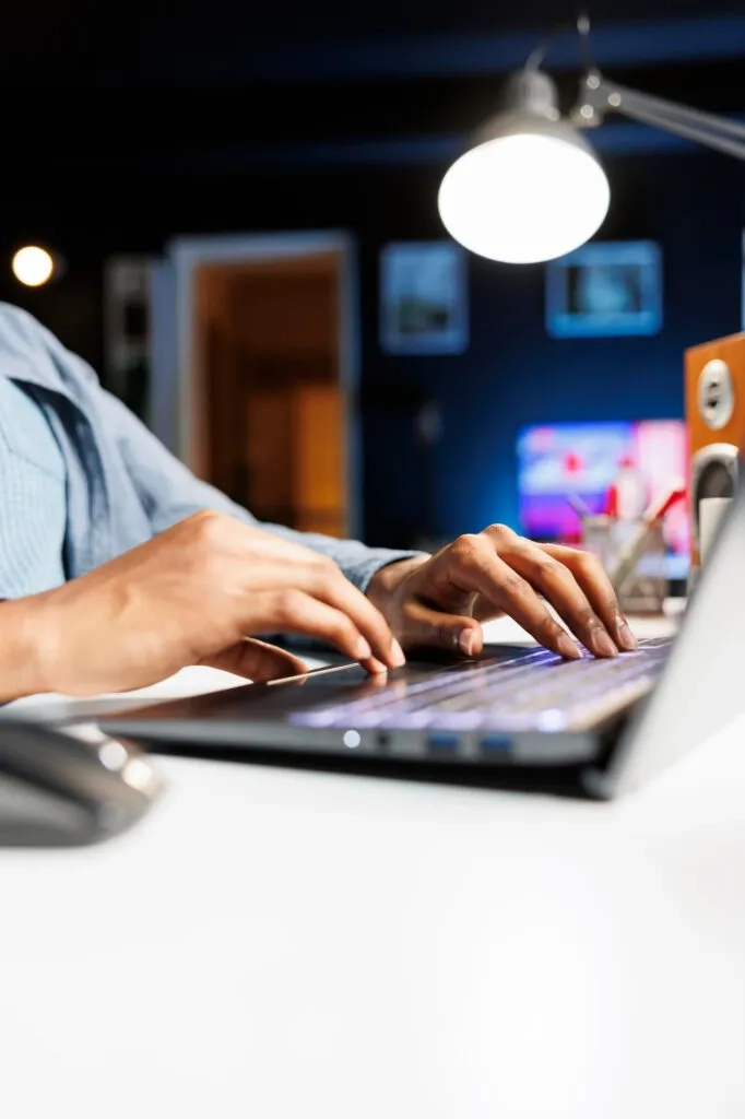 Hands typing on a laptop keyboard under a desk lamp. Law Firm Content Marketing.